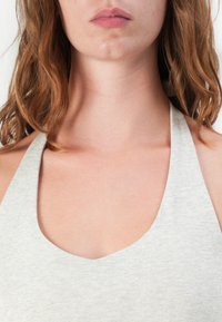 Grijze mouwloze top met een diepe U-vormige halslijn, gemaakt van zacht, gestructureerd materiaal, dat de gladde stof tegen blote huid toont.