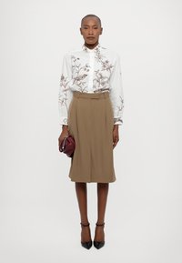 Cămașă albă cu nasturi, decorată cu broderie florală maro, asociată cu o fustă bej până la genunchi. Tocuri înalte negre și o geantă burgundă.
