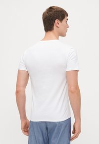 T-shirt blanc à manches courtes avec un col rond, fabriqué en tissu lisse, au design ajusté et à l'ourlet arrière droit.