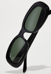 Ochelari de soare negri cu lentile verzi mari și dreptunghiulare. Cadru din plastic elegant, cu un finisaj neted și o branding subtilă pe lentilă.