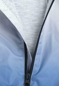 Veste à demi-fermeture éclair avec un tissu dégradé allant du gris clair au bleu, dotée d'une fermeture éclair noire apparente et d'une doublure intérieure grise douce.