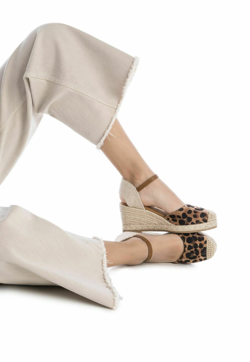 Espadrillas con stampa leopardata, tacco a zeppa e suole in juta intrecciata, con cinturini alla caviglia marroni; abbinate a pantaloni cropped beige larghi con orlo sfrangiato.