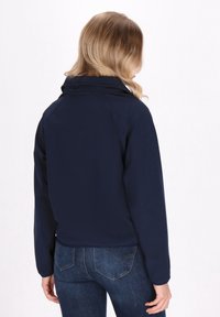 Tamsiai mėlynas švarkas su aukštu apykakle, pagamintas iš lengvos medžiagos. Turi prigludusią siluetą ir rankoves su manžetėmis. Dėvimas su mėlynais džinsais.