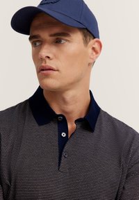 Marineblaues Polo-Shirt mit strukturiertem Muster und kontrastierendem Kragen. Verfügt über drei Knöpfe und eine figurbetonte Passform. Eine blaue Kappe vervollständigt den Look.