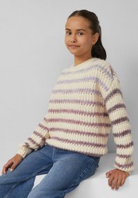 Chunky gebreide trui in crème met lavendel- en donkerpaarse strepen, voorzien van een ronde halslijn en ribbelmanchetten, gecombineerd met lichtblauwe jeans.