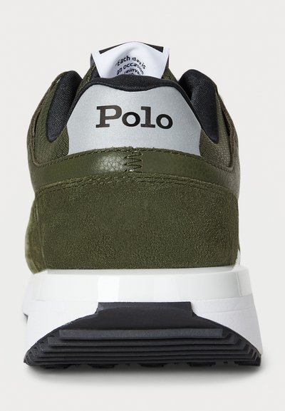 Olijfgroene sneaker met een bovenwerk van suede en synthetisch materiaal, een gepolsterde zwarte kraag, een witte tussenzool en een gestructureerde zwarte loopzool, met een zilveren logoaccent.