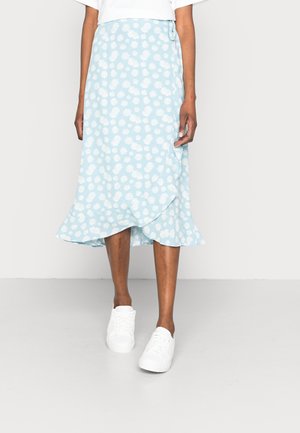 Lichtblauwe midi wikkelrok met witte madeliefjesprint, gedragen met witte sneakers en een wit topje, weergegeven van half torso tot voeten.
