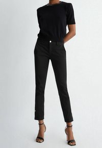 Czarne dopasowane spodnie o smukłym kroju, z kieszeniami z przodu i długości do kostek. W połączeniu z czarną bluzką z krótkim rękawem i sandałami na obcasie.