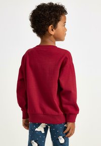 Roter Baumwoll-Sweatshirt mit langen Ärmeln und gerippten Bündchen, kombiniert mit blauen Schlafanzughosen, die weiße Eisbären und Schneeflocken zeigen.