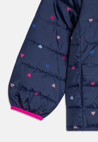 Manche de veste matelassée bleue marine avec motifs de cœurs multicolores, poignet élastique à bordure rose, et texture matelassée pour plus de chaleur.