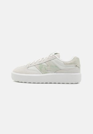 Zapatilla de color claro con un upper de ante y malla texturizados, con un sutil acento verde, cordones planos y una gruesa suela de goma blanca.
