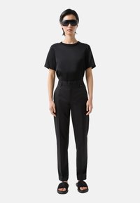 Zwarte kortemouw t-shirt gecombineerd met hooggetailleerde zwarte broek en zwarte sandalen; heeft stijlvolle zonnebril en een minimalistisch ontwerp.