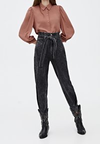Rust-colored satin blouse with puffed sleeves and buttons, paired with high-waisted black denim jeans featuring a tied belt and distressed texture. Black cowboy boots add contrast.