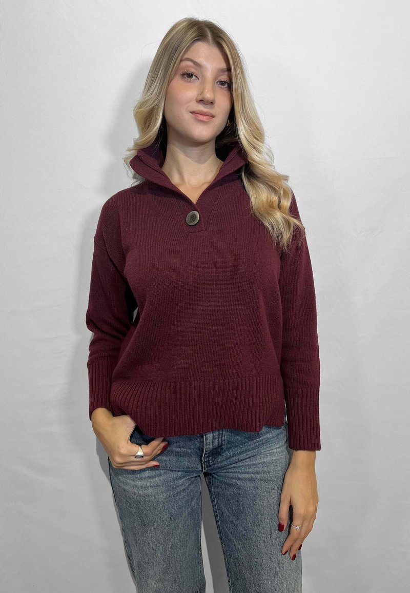 Maglione a maglia borgogna con colletto alto, chiusura con bottoni e polsini a costine, abbinato a jeans in denim azzurri.