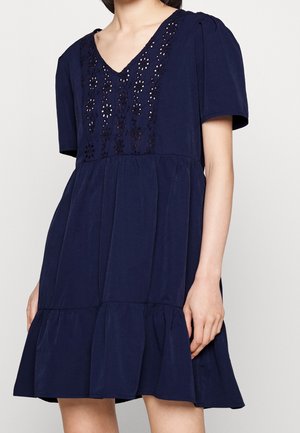 Navy blue short-sleeve dress with V-neck, floral lace cutout detailing on the chest, gathered waist, and flared ruffle hem.