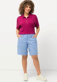 Fialová polokošile s knoflíkovou légou, spárovaná se světle modrými šortkami s předními kapsami. Bílí tenisky dokončují outfit.