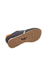 Zapatilla negra y gris con un acento naranja, suela de goma texturizada y entresuela blanca. Presenta un diseño de banda de rodadura para mayor agarre.