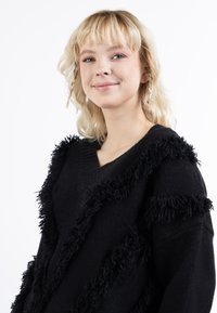 Zwarte trui met een V-halsontwerp en veerkrachtige franjes die verticaal over de voorkant en mouwen lopen. Zachte textuur, ontspannen pasvorm.