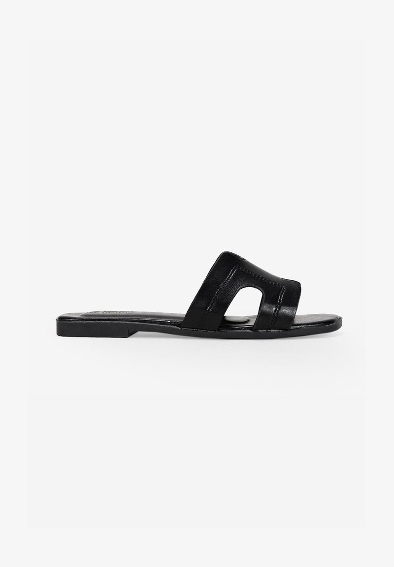 Sandale glissante en cuir noir, avec un bout ouvert, un design à deux lanières avec découpes et une semelle plate. Texture minimaliste et lisse.