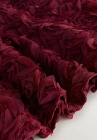 Burgundia kangas kihiliste, lillede kroonlehtede tekstuuridega. Pehme, läbitav materjal loob mõõtmelise ilme õrnade, voolavate detailidega.