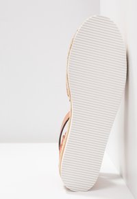 Sandalo con una suola in gomma bianca texturizzata, caratterizzato da una cinghia in pelle marrone e una parte superiore in suede rosa chiaro. Dettaglio di cuciture sui bordi visibile.