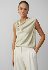 Satin ärmelloses Top in hellem Creme mit drapiertem Ausschnitt. Kombiniert mit maßgeschneiderten, cremefarbenen Hosen mit Reißverschluss-Tasche.