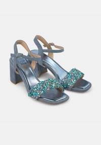 Blauwe blockhak sandalen met een metallic afwerking en enkelbandjes, met een versierde band van turquoise en zilveren stenen aan de voorkant.