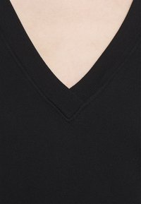 Suéter negro de cuello en V con un escote acanalado, textura suave y diseño ajustado, que muestra una apariencia limpia y minimalista.