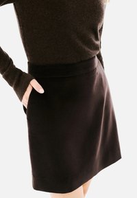 Jupe noire en tissu lisse avec une taille ajustée et des poches. Le design présente une silhouette épurée et simple.