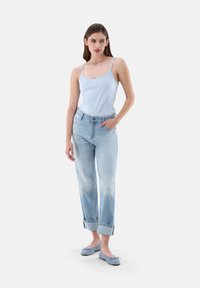 Hellblaues Tanktop, verblasste blaue Jeans mit aufgerolltem Saum und hellblauen flachen Schuhen. Hat eine lässige Passform und ein entspanntes Design.