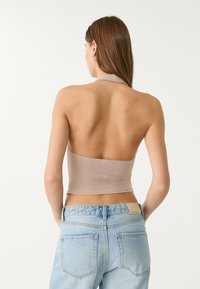 Bakvy av en åtsittande, ärmlös topp i ljusbeige, med halterneck och en slät, strukturerad yta, tillsammans med högmidjade ljusa jeans.