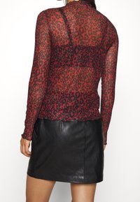 Röd nättröja med långa ärmar och svart leopardmönster, med en scalloped nederkant och genomskinlig textur, ihop med en svart läderminikjol.