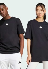 Svarta bomull t-shirts med korta ärmar, med en vit triangulär logotyp på övre vänster bröst. Enkel, avslappnad passform.