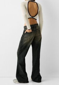 Vit ribbad långärmad crop top med stor skärning på ryggen, i kombination med svarta vida byxor i jeansmaterial med ett blekt utseende och sömdetaljer.