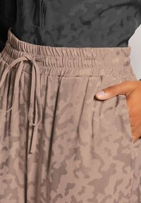 Hellbraune Sweatpants mit einem dezenten Camouflage-Muster, elastischem Bund mit Kordelzug und seitlichen Taschen. Strukturiertes Stofffinish.