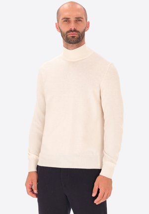 Maglione a collo alto crema realizzato in morbido tessuto. Presenta maniche lunghe, polsini a coste e una texture liscia. Abbinato a pantaloni scuri.