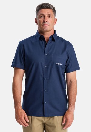 Kurzärmeliges, hemdenartiges Shirt aus dunkelblauem Stoff mit einer Brusttasche, die ein kleines Logo aufweist. Glatte Textur, klassisches Kragen Design.