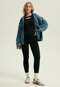 Czarne, dopasowane legginsy połączone z luźną niebieską kurtką dżinsową, czarnym topem z wykrojem oraz białymi skarpetkami i trampkami.