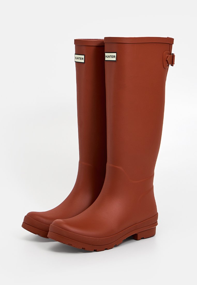 Bruine rubberen tot de knie hoge regenlaarzen met een gladde textuur, platte zool en verstelbare riemdetails nabij de bovenkant. Voorzien van logo-merken.