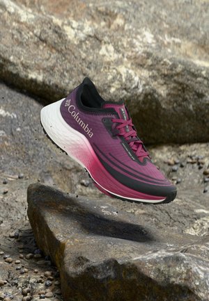 Μπορντό και μαύρο sneaker Columbia με λευκή σόλα που αιωρείται πάνω από πετρώδες έδαφος, παρουσιάζοντας ελαφρύ σχεδιασμό για τρέξιμο σε μονοπάτια.
