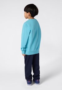Sweatshirt azul claro com mangas e bainha ajustadas, combinado com calças de treino azul marinho. O calçado apresenta uma base azul com detalhes em vermelho.