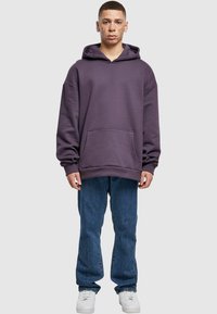Felpa oversized viola con tasca frontale, abbinata a jeans blue dritti e sneakers bianche. Tessuto morbido con vestibilità comoda.