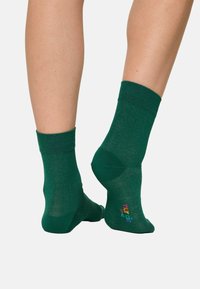 Calze verdi realizzate in un morbido materiale testurizzato, con un polsino a costine e un logo multicolore sulla suola. Lunghezza standard alla caviglia.