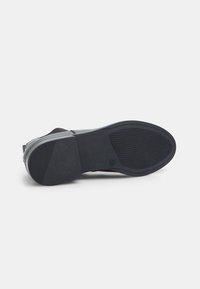 Suela de zapato negra con textura de goma antideslizante, forma angular y área del talón reforzada, con un acabado liso y un diseño minimalista.