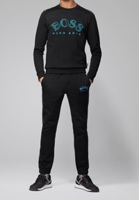 Completo felpa nera e pantaloni con logo "BOSS" azzurro chiaro, realizzato in tessuto morbido, con scollo a girocollo e polsini elasticizzati, abbinato a sneakers.