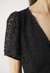 Vestido negro de encaje con un delicado patrón floral, mangas cortas y escote en V, que muestra un diseño de tela texturizada y transparente.