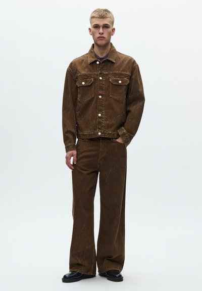 Set din denim maro, jachetă și pantaloni, cu textură estompată. Jacheta are două buzunare pe piept și nasturi argintii. Pantalonii evazați completează ținuta.