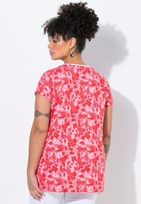 Top corto de manga corta con patrón floral rojo, hecho de una tela suave. El diseño presenta una mezcla de flores grandes y pequeñas sobre un fondo rosa.