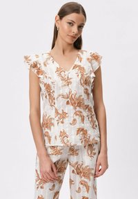 Biała bluzka z pomarańczowym kwiatowym wzorem, dekoltem w serek i falbaniastymi krótkimi rękawami; zestawiona z pasującymi spodniami w ten sam wzór, lekkiego materiału i luźnym kroju.