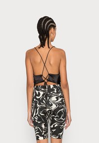 Top cropped de satin preto com laços cruzados nas costas, combinado com calções de bicicleta de altura alta em preto e branco com padrão marmoreado. Textura suave.